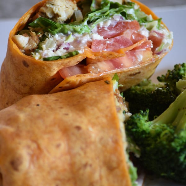 Chicken wrap with lettuce, tomatoes, and feta cheese, served with a side of broccoli.
