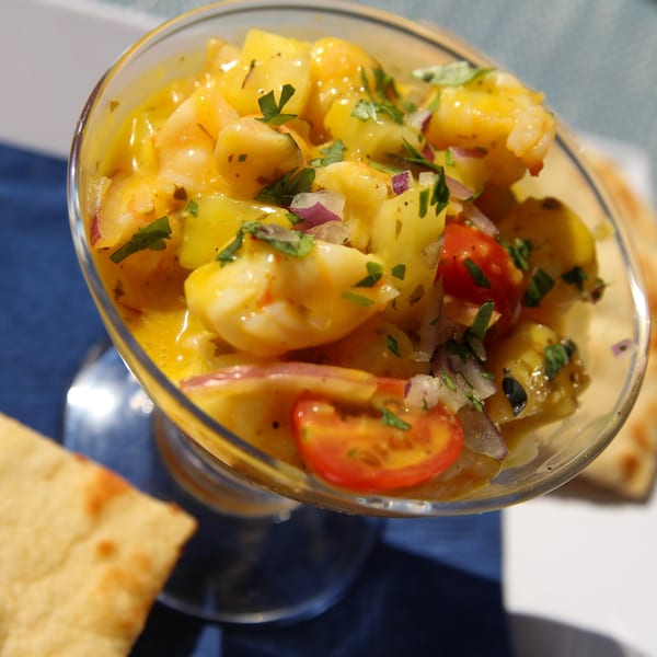 Close-up of shrimp ceviche with mango, cherry tomatoes, red onion, and cilantro in a glass.