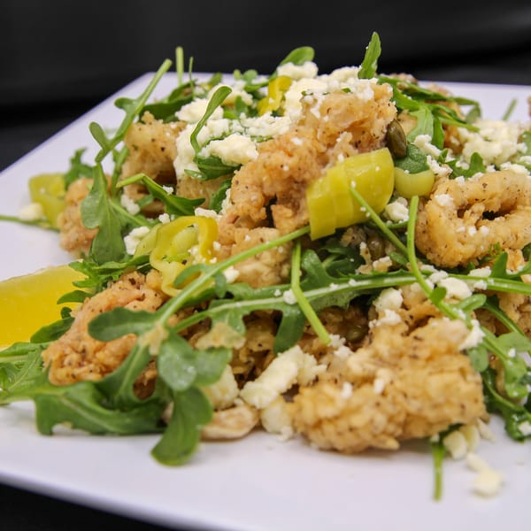 Fried calamari salad with arugula, feta cheese, banana peppers, and a lemon wedge.