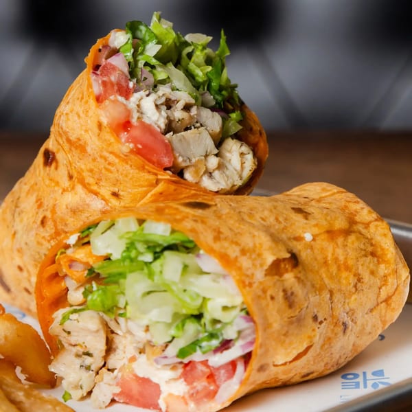 Two chicken gyros wraps, filled with chicken, lettuce, tomatoes, and sauce, on a white plate.