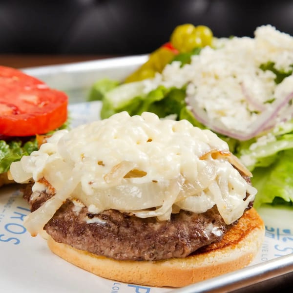 Spiro's Taverna burger with melted cheese and caramelized onions, served with a side salad.