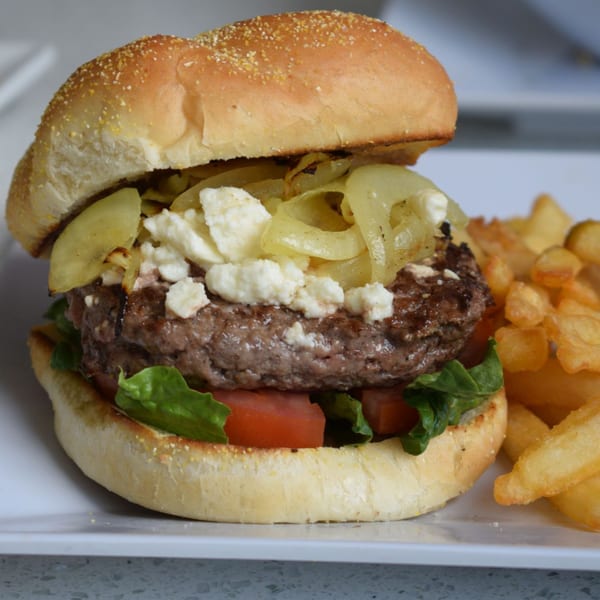 Gourmet burger with caramelized onions, feta cheese, lettuce, and tomato, served with fries.