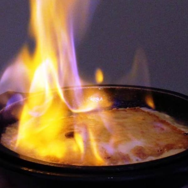Flambéed dish in a black pan, with bright yellow and purple flames rising from the food.