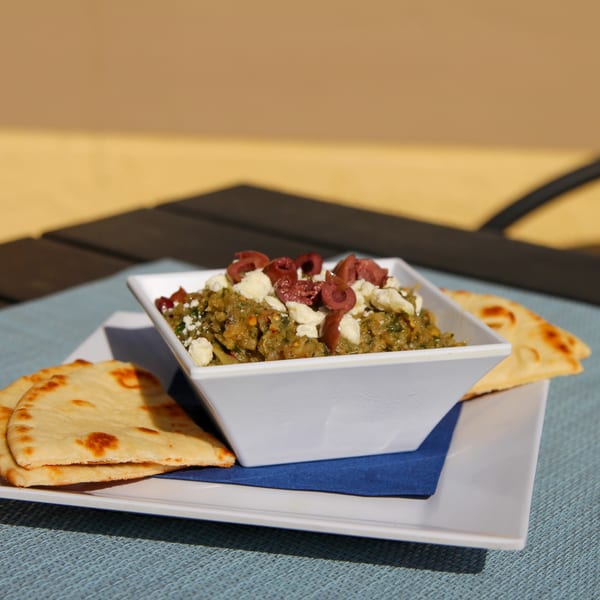 Spiro's Taverna's eggplant dip with feta and olives, served with pita bread on a white plate.