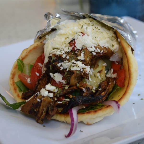 A pita wrap filled with grilled vegetables, feta cheese, and herbs, partially wrapped in foil.