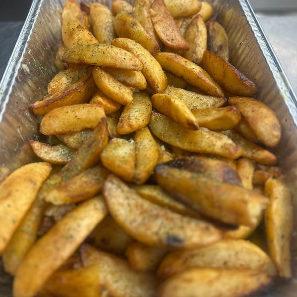 Golden-brown potato wedges seasoned with herbs and spices, served in a foil container.