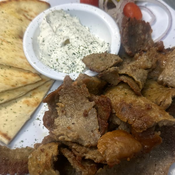 A close-up of a gyro platter with sliced meat, pita bread, tzatziki sauce, and vegetables.
