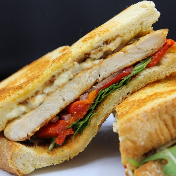 Grilled chicken sandwich with roasted red peppers, lettuce, and cheese on toasted bread.