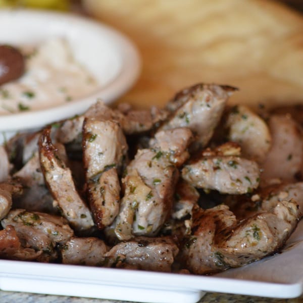 Close-up of seasoned pork chunks on a white platter, with a blurred dip in the background.