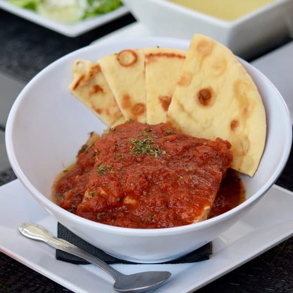 Saganaki in a white bowl, topped with red sauce and herbs, served with pita bread.