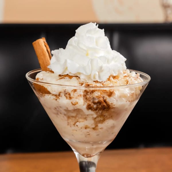 Greek rice pudding with whipped cream, cinnamon, and a cinnamon stick in a martini glass.