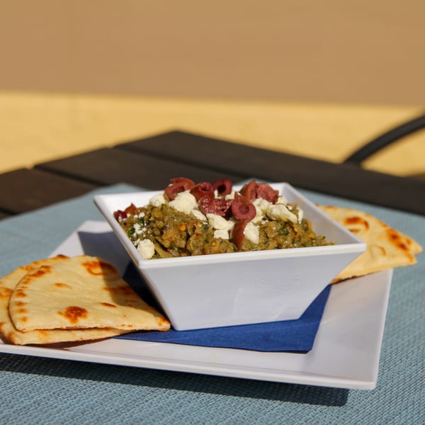 Spiro's Taverna's Greek dip with olives and feta, served with pita bread on a white plate.